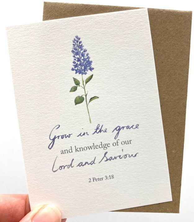A hand holding the notecard with a flower design and the scripture text